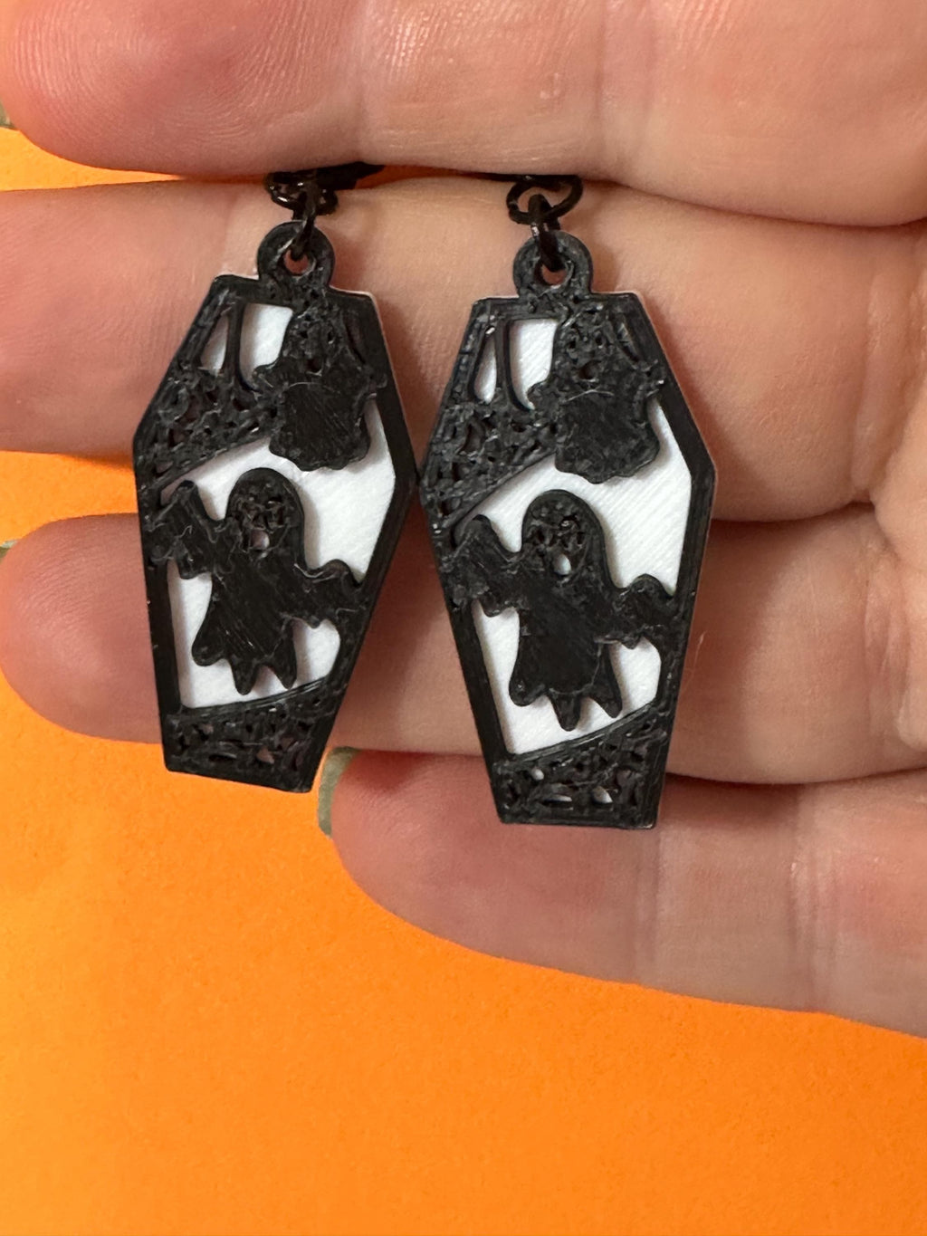 Black ghost coffin dangle earrings with translucent white backing, held in hand