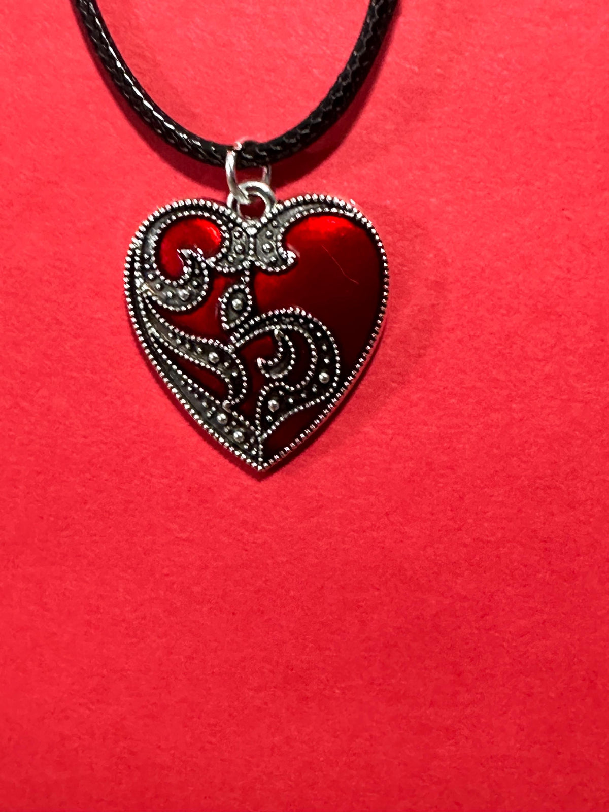 Close-up of red heart pendant with silver filigree scrollwork on black cord