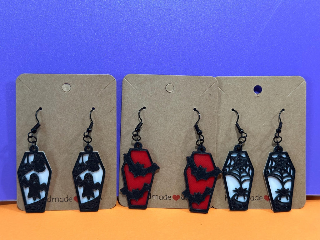 Three pairs of coffin earrings on display cards: ghost, bat, and spiderweb designs