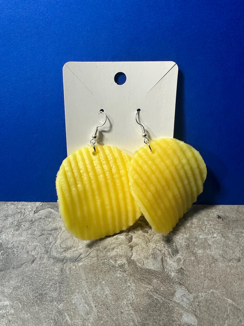 Yellow ruffled chip earrings on earring card with stone surface below