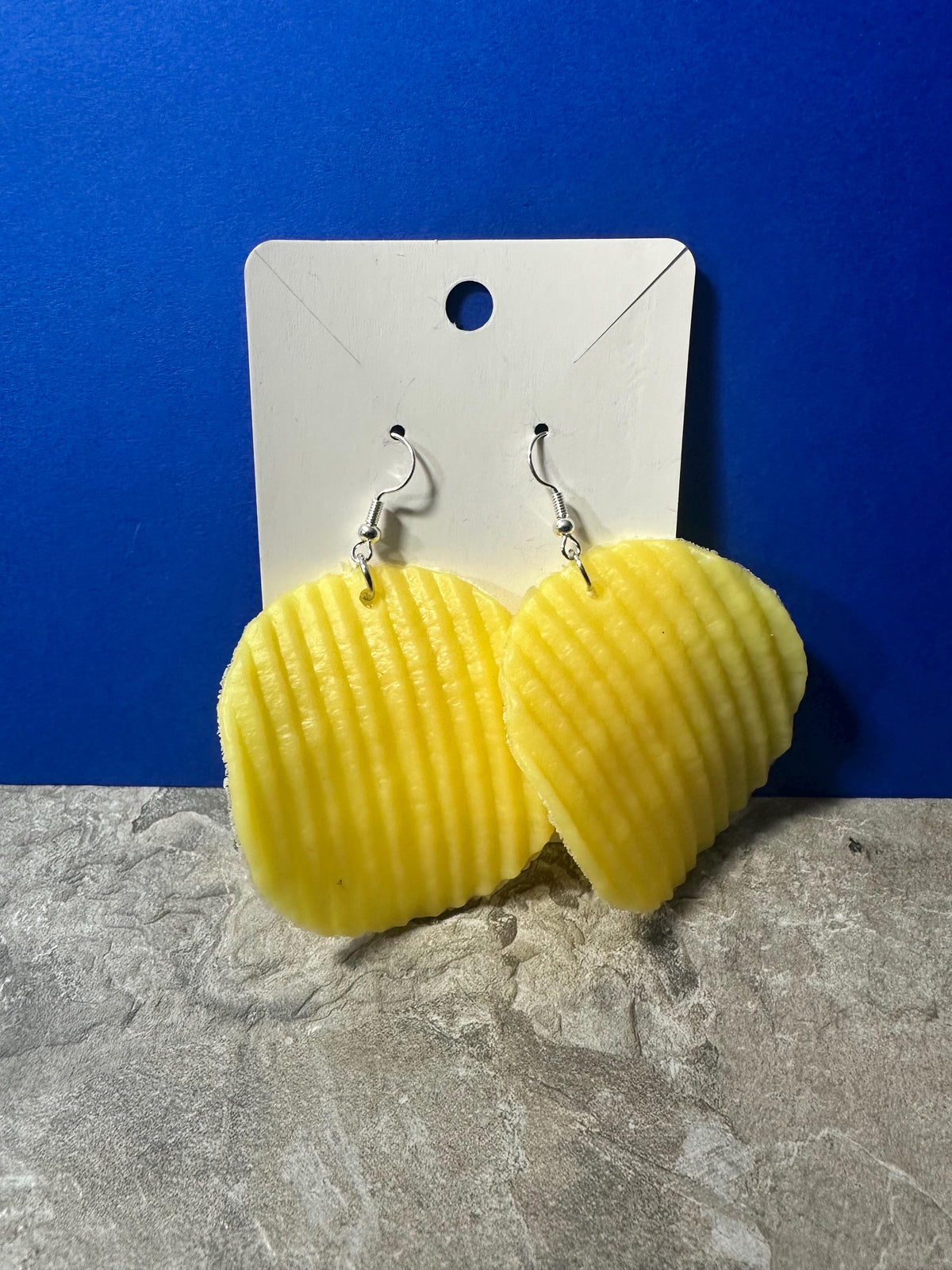 Yellow ruffled chip earrings on earring card with stone surface below