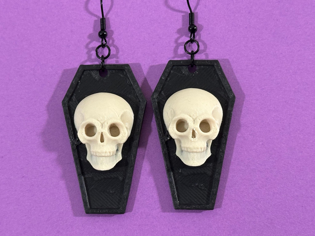 Skull coffin statement earrings displayed on purple background