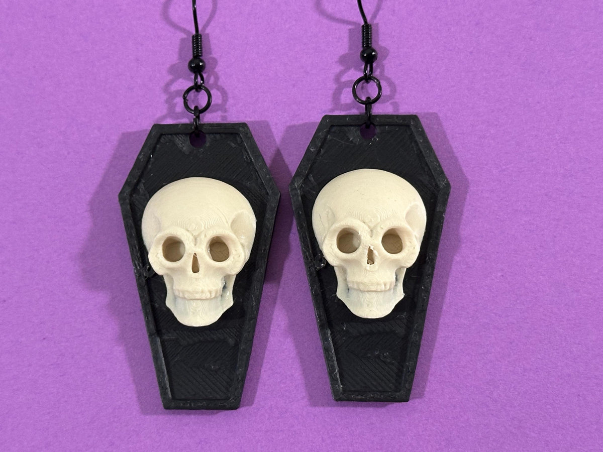 Skull coffin statement earrings displayed on purple background