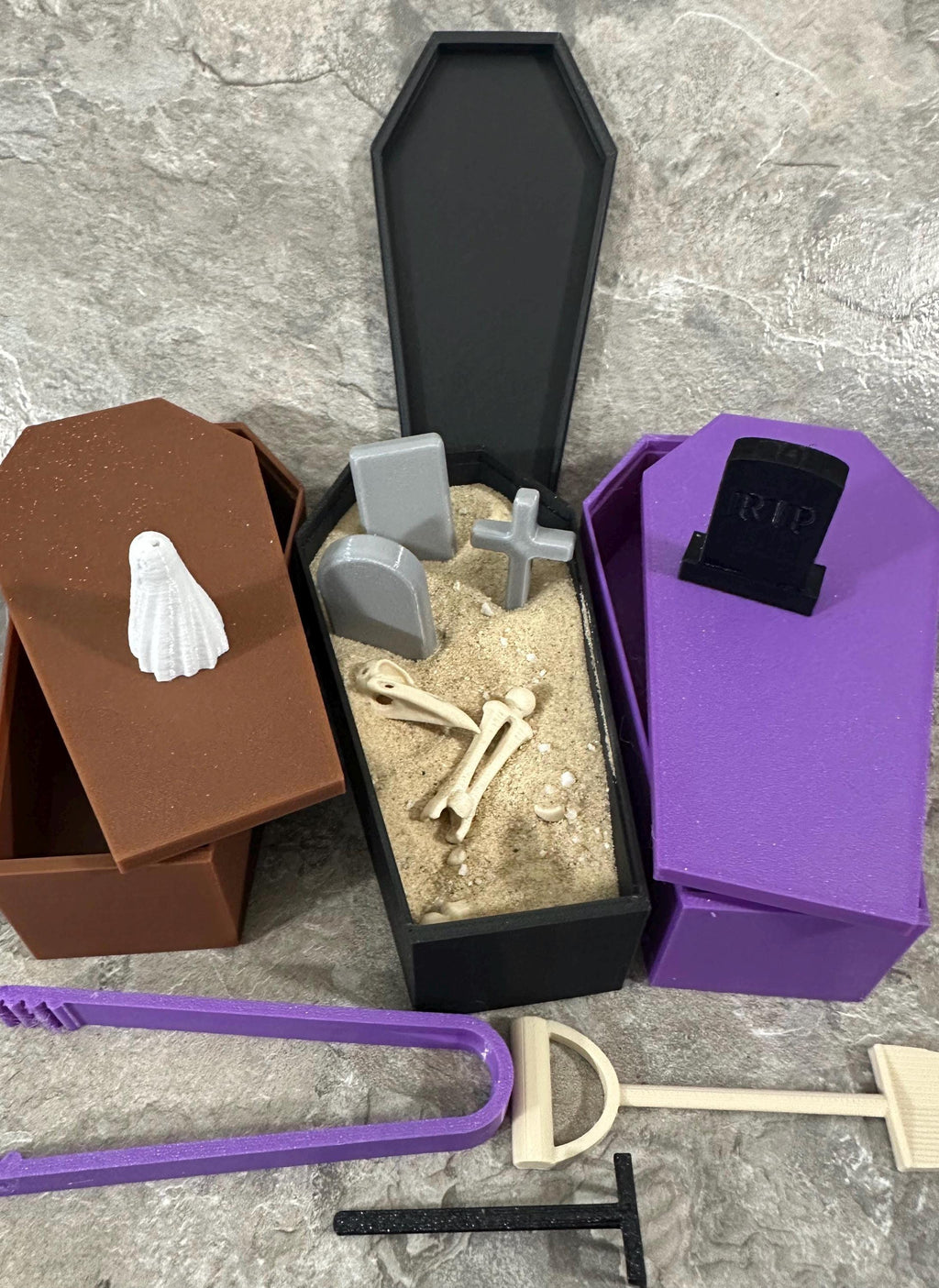Black coffin zen garden filled with sand, tombstones, cross and skeleton bones