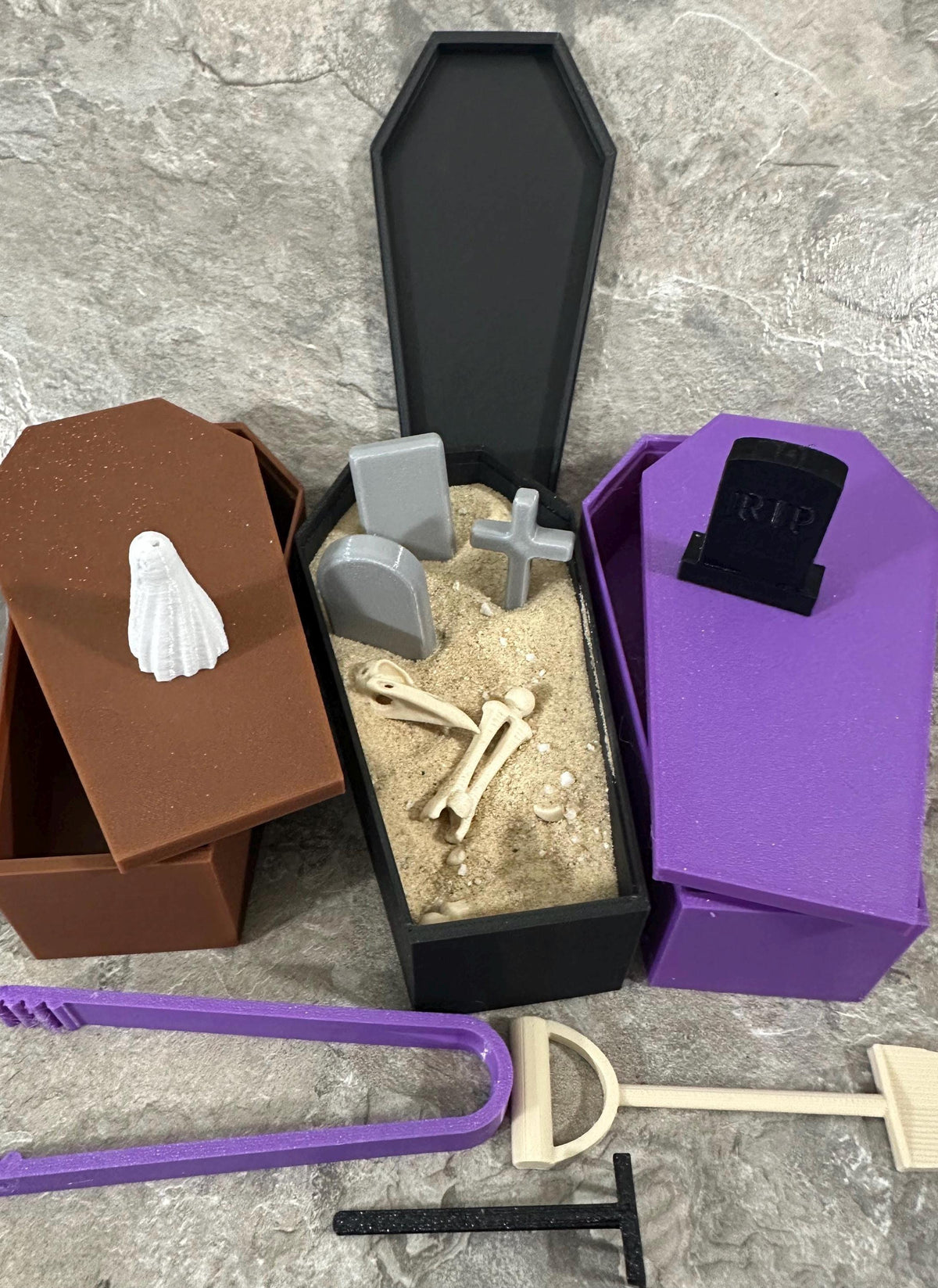 Black coffin zen garden filled with sand, tombstones, cross and skeleton bones