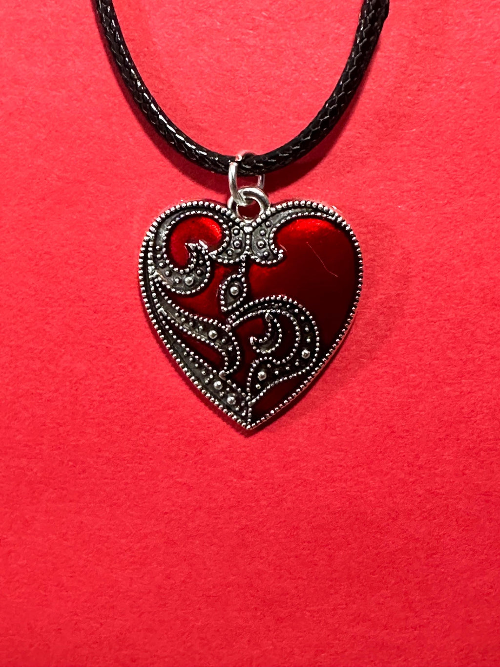 Red enamel heart pendant with silver scrollwork on black cord, close-up on red