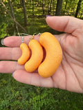 Hand holding three sizes of 3D printed cheese puff earrings, small medium and large, outdoors with trees behind