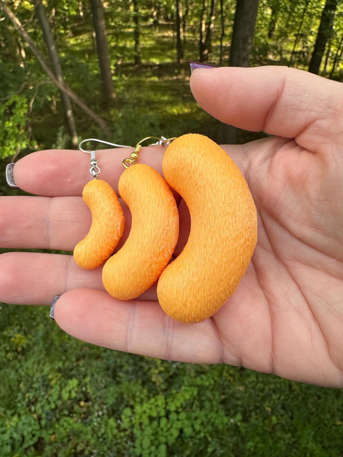 Hand holding three sizes of 3D printed cheese puff earrings, small medium and large, outdoors with trees behind