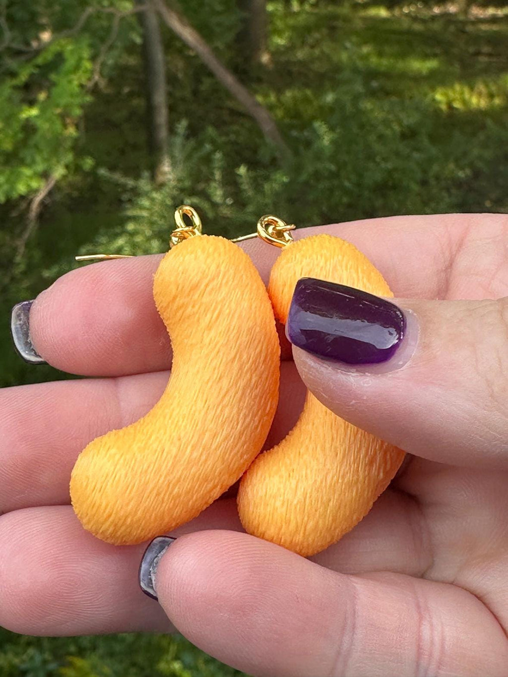 Close-up of two large 3D printed cheese puff earrings with gold hooks held between fingers