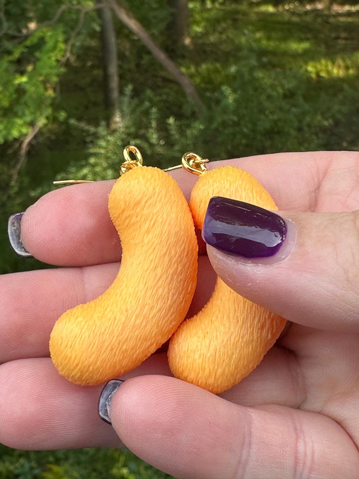 Close-up of two large 3D printed cheese puff earrings with gold hooks held between fingers
