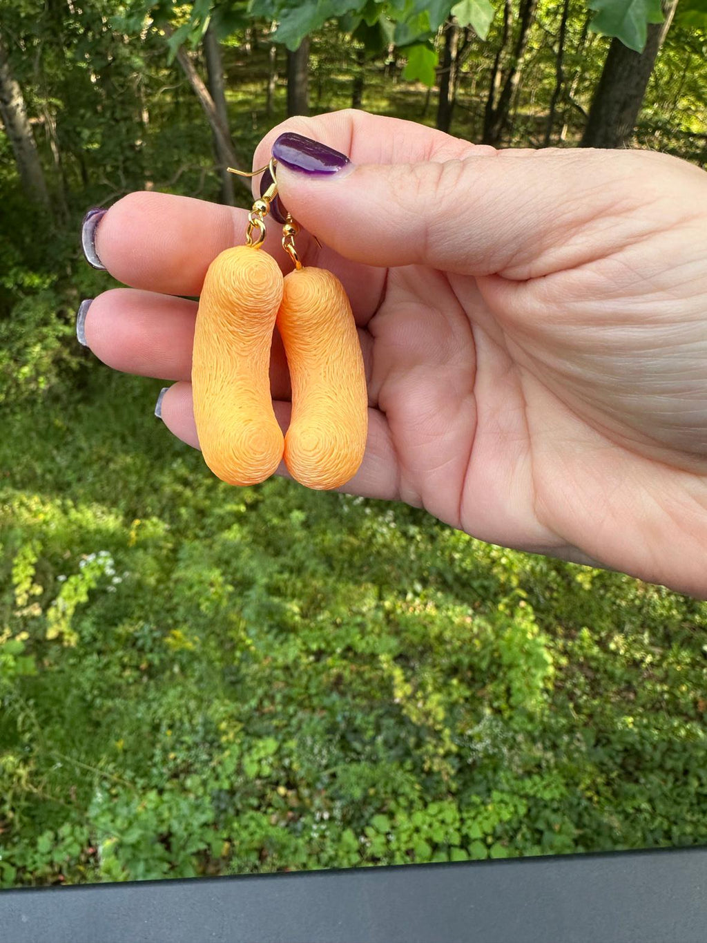 Pair of medium 3D printed cheese puff earrings with gold hooks held up outdoors