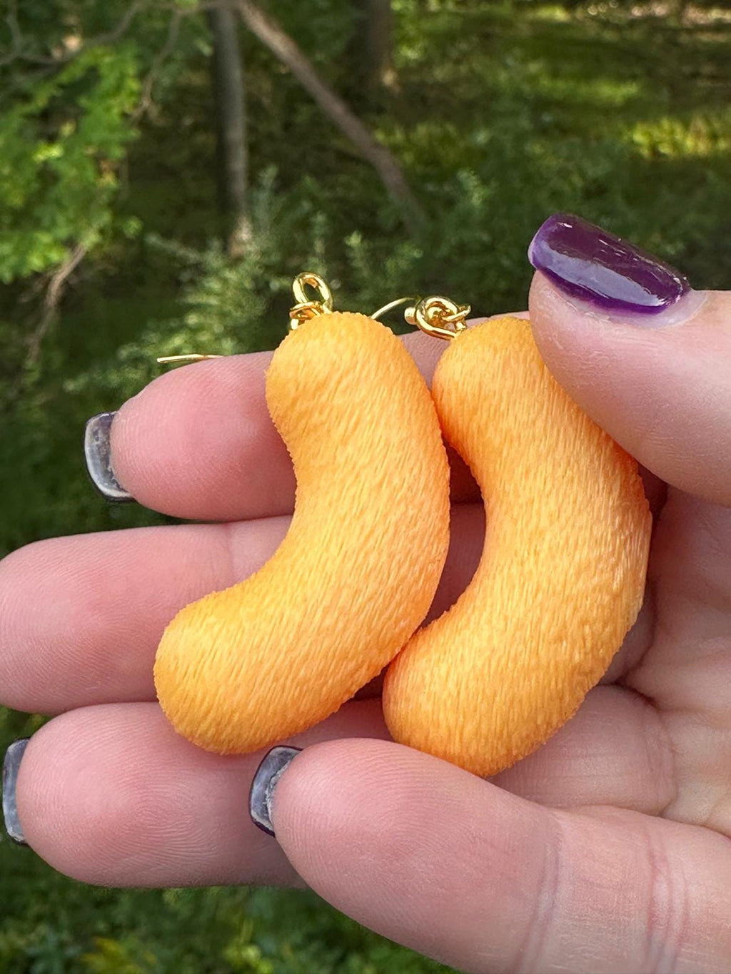 Two large 3D printed cheese puff earrings with gold hooks resting in an open hand