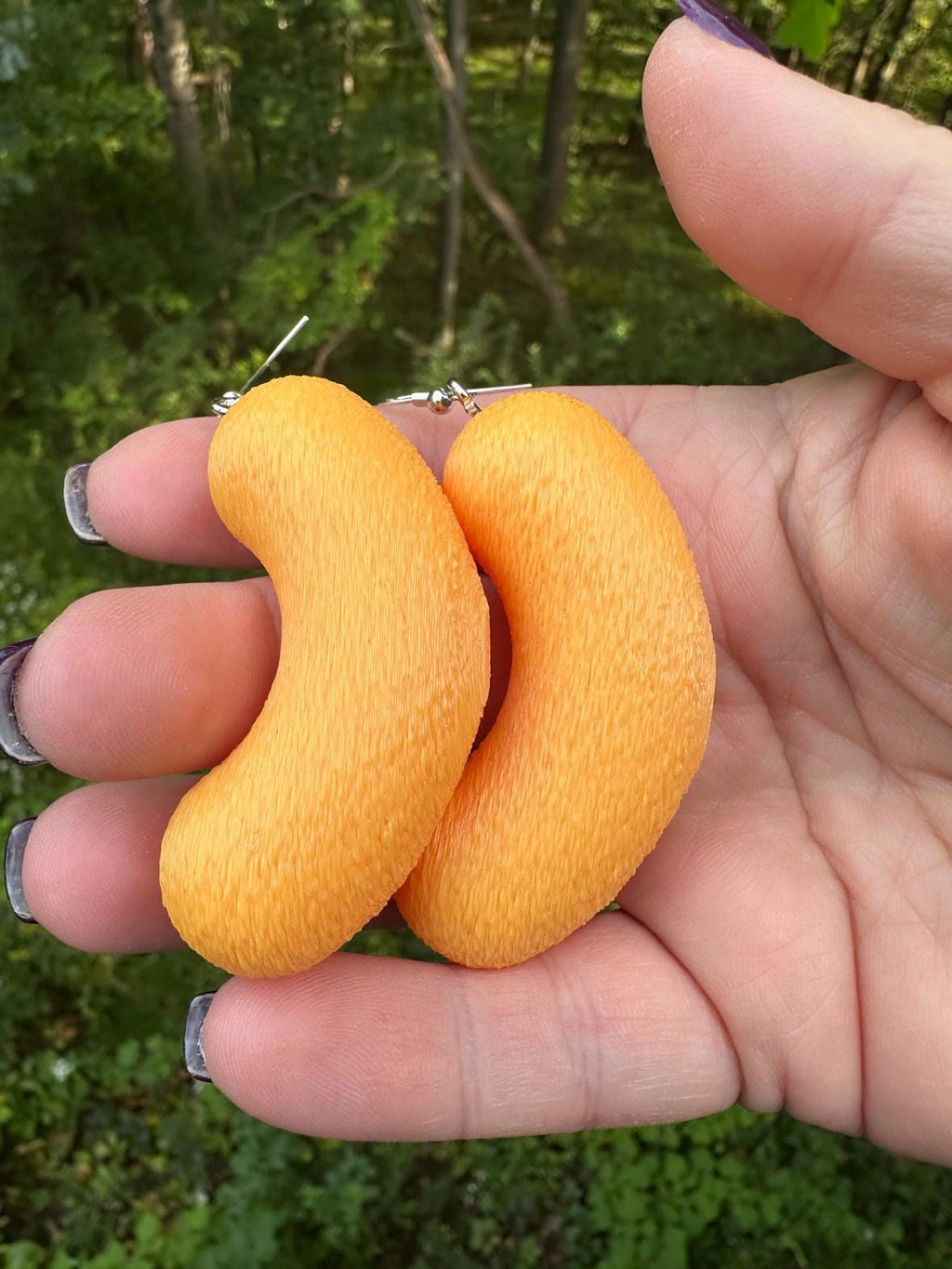 Two large orange 3D printed cheese puff earrings with silver hooks showing textured surface in hand