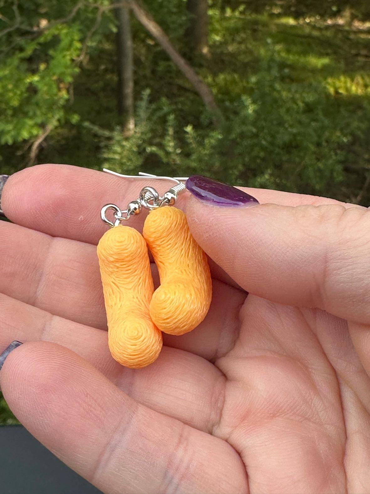 Two small 3D printed cheese puff earrings with silver hooks showing printed layer texture in hand