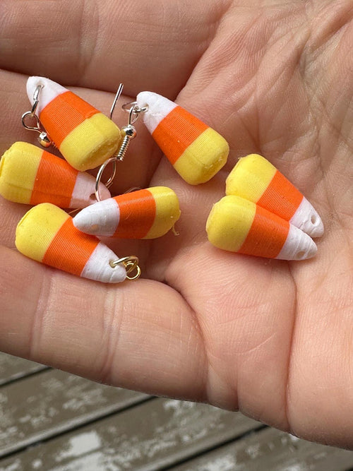 3D printed candy corn charms in open palm, two with silver and gold earring hooks