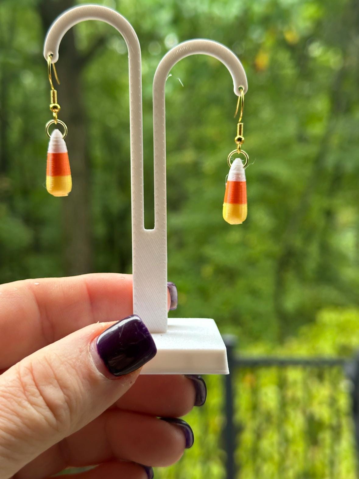 Candy corn dangle earrings with gold hooks on white stand, held outdoors