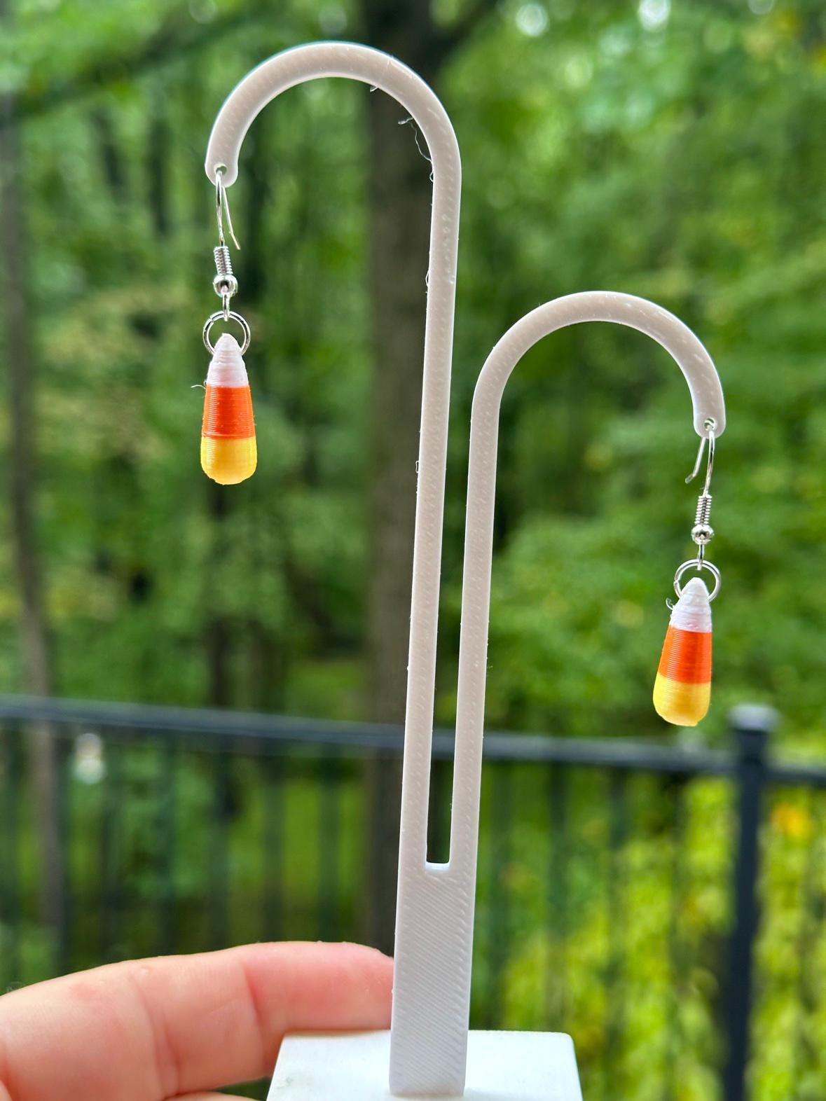 Candy corn earrings with silver hooks hanging on white stand outdoors
