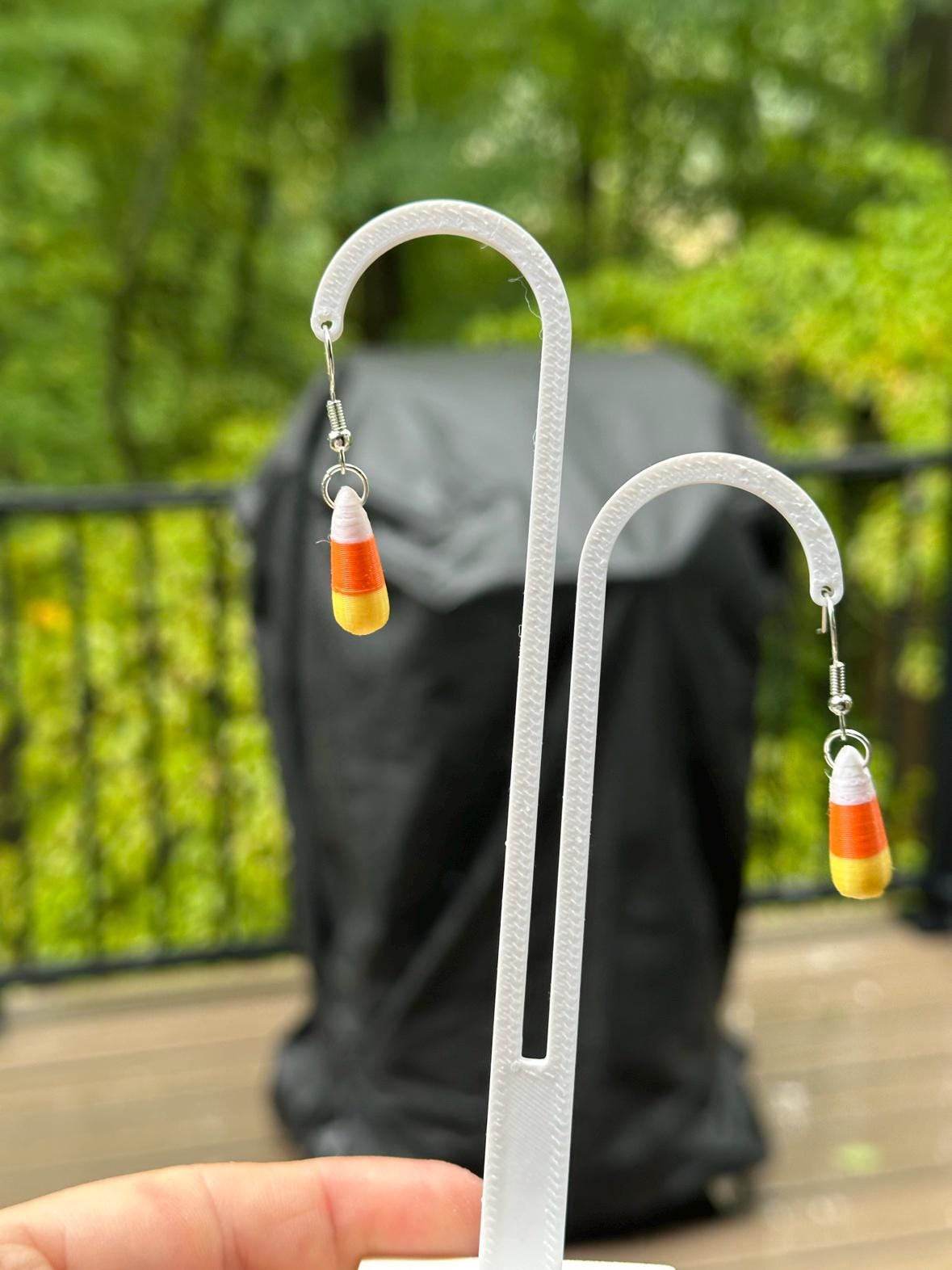 3D printed candy corn dangle earrings on stand, outdoor patio background